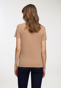 Beżowa koszulka z krótkim rękawem, wykonana z gładkiego, elastycznego materiału, z okrągłym dekoltem. Noszona z ciemnoniebieskimi dżinsami, prezentującymi prosty, schludny design.