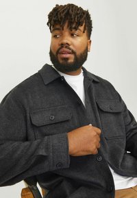 Gray button-up shirt jacket with two chest pockets and a classic collar, featuring a textured fabric and adjustable cuffs.