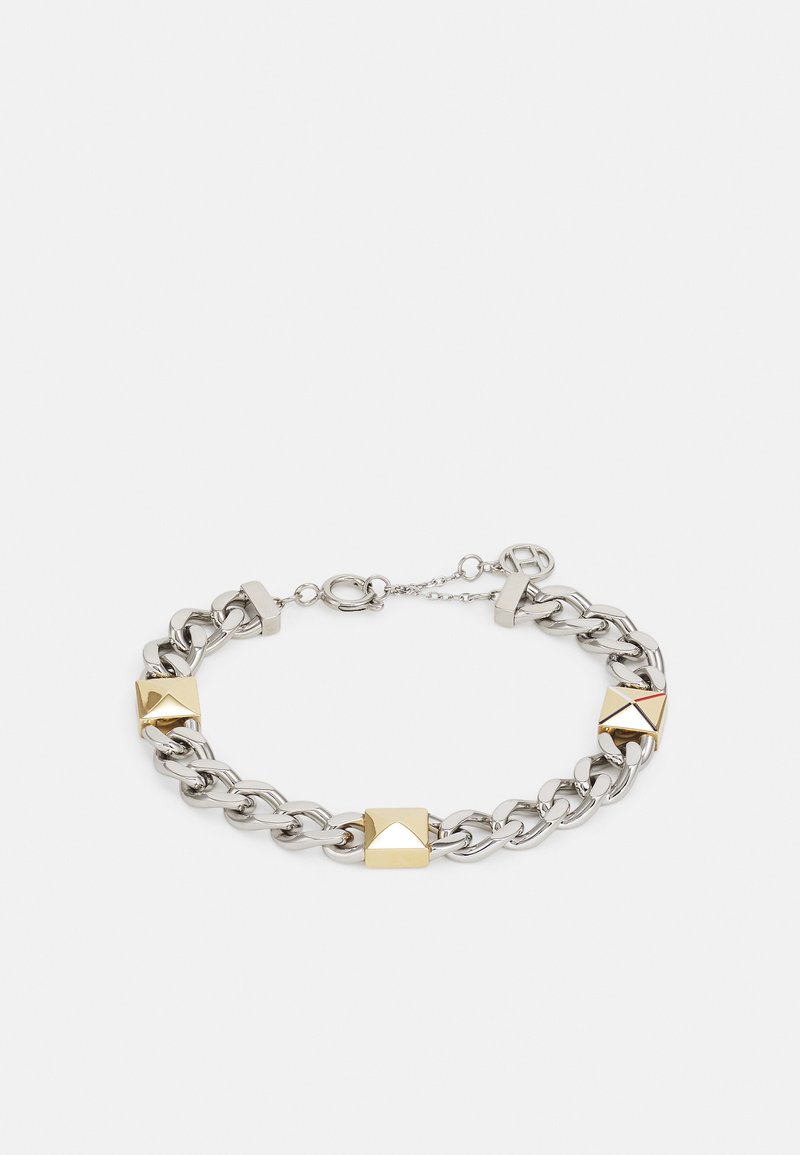 Pulsera de cadena metálica plateada que presenta acentos en forma de pirámide dorados, un cierre de palanca y una longitud ajustable. Textura suave y brillante.