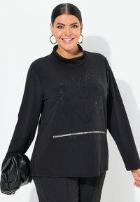 Svart långärmad tröja med en cowl-hals, glittrig blommönster och texten "BLOOM YOUR OWN WAY" med en silveraccentband.