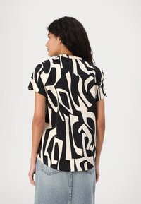 Svart og beige kortermet topp med abstrakt design, glatt tekstur, rund halslinning og en lett buet hemline.
