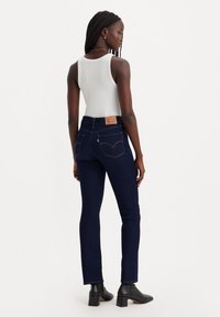 Jeans in denim blu scuro con vita alta, taglio dritto e design classico delle tasche posteriori. Indossati con un top fitted bianco e stivaletti neri alla caviglia.