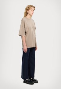 T-shirt beige oversize con maniche corte, caratterizzato da un accento circolare, abbinato a pantaloni navy a gamba larga e scarpe con plateau nere.