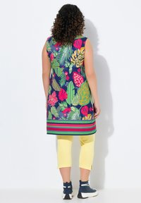 Kwiatowa tunika w granatowym kolorze z wielokolorowymi tropikalnymi wzorami, w połączeniu z żółtymi spodniami capri. Posiada paskowany krój u dołu oraz bezrękawowy design.