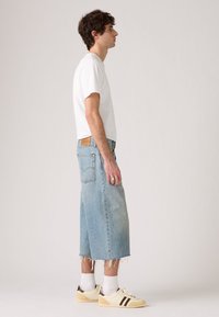 Pantalones cortos de mezclilla azul claro con dobladillo deshilachado, combinados con una camiseta blanca y zapatillas crema con rayas marrones en los lados.