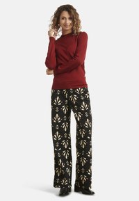 Red long-sleeve sweater with a crew neckline paired with black wide-leg pants featuring a cream floral pattern and black heeled boots.
