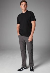 Sort kortærmet t-shirt parret med grå lige ben bukser og sorte sneakers med hvide striber, mod en neutral baggrund.