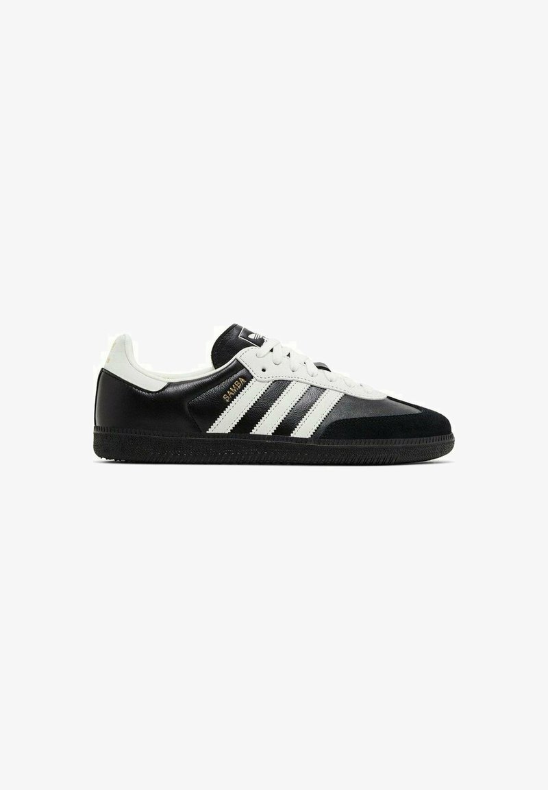 Baskets Adidas Samba en noir et blanc avec trois bandes blanches, semelle noire, lacets blancs et inscription dorée "SAMBA" sur le côté.