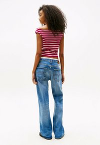 Top a righe rosse e bianche senza spalline, abbinato a jeans a vita alta svasati blu con tasche posteriori e una texture sbiadita.
