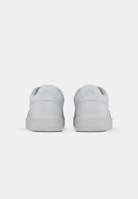 Light gray sneakers with a smooth leather upper, rounded heel, and minimalistic design. Features a textured rubber sole and subtle logo detailing.