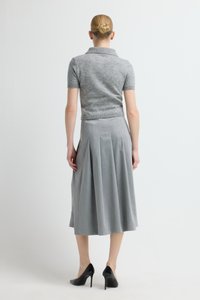 Lichtgrijze, gebreide top met korte mouwen gecombineerd met een grijze, geplooide rok van middellange lengte. Het model draagt zwarte hoge hakken. Effen achtergrond.