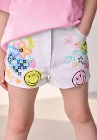Pantaloncini in denim bianco con motivi stampati multicolori, tra cui faccine sorridenti, fiori e cuori. Dotati di due tasche laterali.