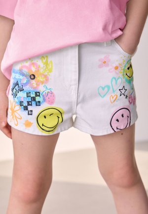 Hvide denimshorts med flerfarvede trykte mønstre, herunder smileys, blomster og hjerter. To sidelommer inkluderet.