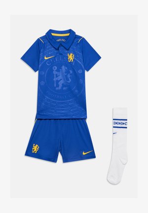 Blauw Chelsea voetbaltenue met poloshirt, korte broek en witte sokken met gele Nike-logo's en clubleeuwenembleem.