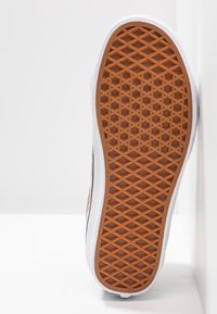 Semelle de chaussure en caoutchouc avec un motif de diamant marron, bords blancs et une texture subtile. Le design présente des impressions florales vives sur les côtés.