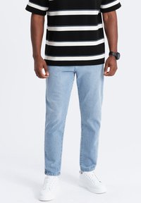Camisa de manga corta a rayas en blanco y negro, jeans de color azul claro y zapatillas blancas. La camisa tiene una tela texturizada y un corte relajado.