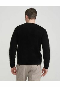 Schwarzer, flauschig gestrickter Pullover mit langen Ärmeln und einem gerippten Bündchen. Die Rückseite verfügt über einen runden Ausschnitt und eine strukturierte Oberflächenbeschaffenheit. Kombiniert mit hellen Hosen.