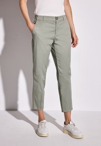 Pantalons cropped vert clair en tissu doux, dotés de poches latérales et d'une fermeture à bouton, associés à des baskets blanches.
