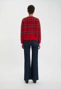 Pull-over à carreaux rouges avec un col rond et un ourlet côtelé, associé à un jean noir à pattes d'éléphant. Le tissu semble doux et texturé.