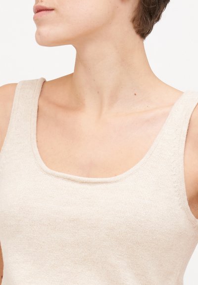 Μπεζ πλεκτό τοπ με απαλή υφή. Διαθέτει φαρδιές τιράντες και στρογγυλή λαιμόκοψη, αναδεικνύοντας ένα μινιμαλιστικό σχέδιο.