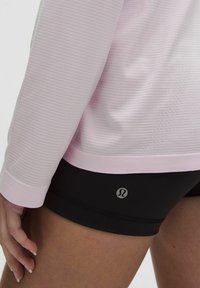 Bluză roz cu mânecă lungă, cu dungi texturate, asortată cu pantaloni scurți negri cu un logo. Material neted, cu o croială ajustată.