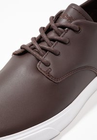 Baskets en cuir marron à bout rond, avec surpiqûres décoratives et lacets marron. Semelle en caoutchouc blanc avec détails texturés. Logo embossé sur le côté.