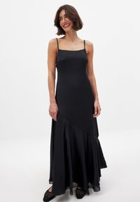 Mustapitu maxi-mekko, jossa on ohuet hihnat, sileä satiininen pinta, epäsymmetrinen helma ja kerrostettu hame. Huomionarvoinen yksinkertaisesta, elegantista muotoilustaan.