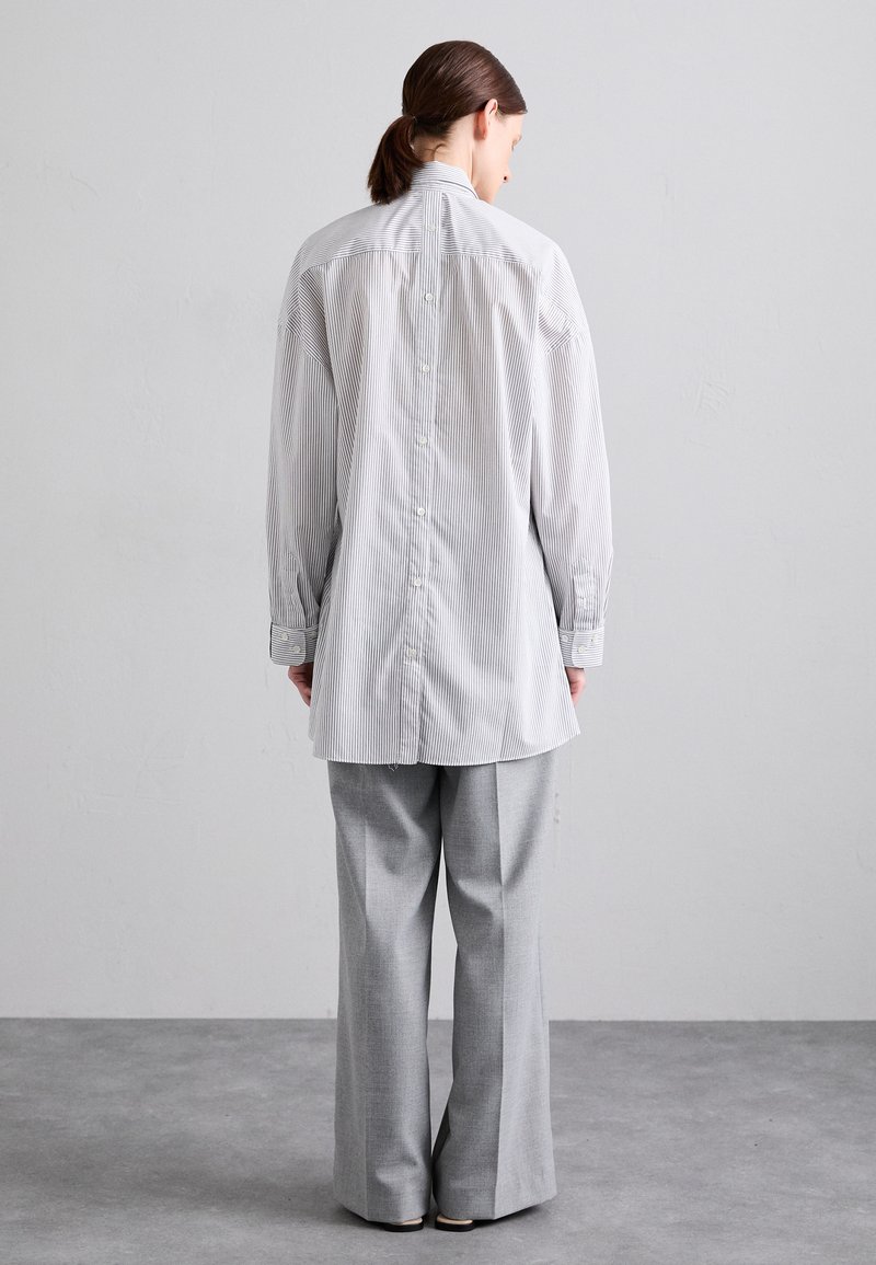 Chemise rayée à manches longues avec un col haut, boutons dans le dos, associée à un pantalon gris à jambes larges. Texture de tissu lisse.