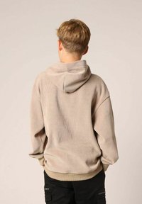 Hoodie beige côtelé avec une capuche à cordon, coupe oversized et poignets élastiques. Porté avec un pantalon cargo noir avec des détails zippés.