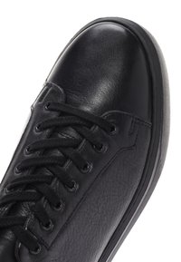 Sneaker in pelle nera con una finitura liscia e lucida. Presenta lacci tondi, occhielli in metallo e una superficie testurizzata lungo i lati.