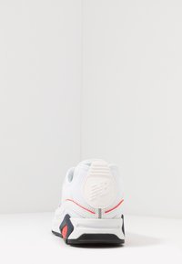 Bílé síťované tenisky s polstrovaným límcem, červeným akcentním pruhem a gumovou podrážkou se černou a oranžovou částí na patě.