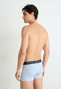 Helles blaues Baumwoll-Boxershorts mit einem schwarzen Bund, auf dem der Markenname "GANT" in Weiß aufgedruckt ist. Glatte Textur, enganliegendes Design.