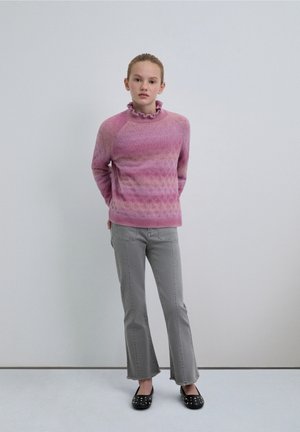 Pull tricot rose avec un col festonné, un motif texturé et un dégradé de couleurs ; associé à un jean évasé gris clair et des ballerines noires.