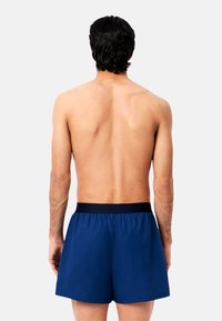 Shorts de bain bleu marine avec une taille élastique, en tissu léger et doux, offrant une coupe décontractée, vus de dos.