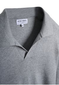 Polo shirt in misto cashmere grigio con colletto a V, vestibilità regolare, caratterizzato da una texture morbida e da un leggero ribbing sul colletto. Etichetta del marchio visibile.