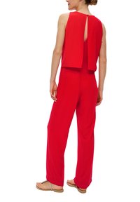 Roter ärmelloser Jumpsuit mit einem Schlüsselaugen-Detail im Rücken, weit geschnittenen Beinen und leichtem Material, das minimale Nähte und keine sichtbaren Muster aufweist.