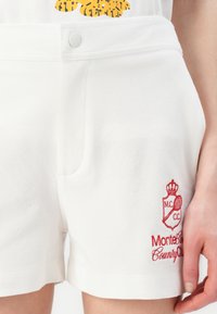 Biele bavlnené šortky s textúrovaným povrchom. Majú predný gombík, dve bočné vrecká a červené vyšívané logo.
