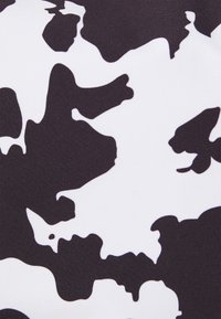 Tessuto a stampa mucca in bianco e nero con una texture liscia, caratterizzato da grandi forme astratte su uno sfondo uniforme.