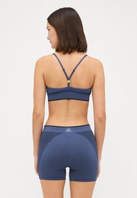 Navy blue sports bra with adjustable straps and a textured design. Paired with matching fitted shorts featuring subtle stripes and brand logo.