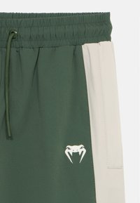 Πράσινο και μπεζ παντελόνι φόρμας με ελαστική μέση, με κορδόνι, πλαϊνή τσέπη και λευκό κεντητό λογότυπο καβουριού. Μαλακή, λεία υφή.