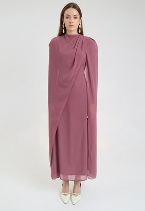 Long, mauve dress with draped fabric, high neckline, and fitted silhouette. Features a side slit and sheer overlay, paired with white pointed heels.