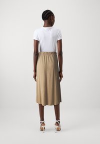 Top bianco a maniche corte abbinato a una gonna beige lunga fino al polpaccio, con vita elastica e una texture liscia e morbida. Sandali bianchi con tacco.
