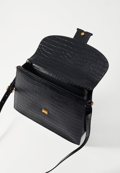 Borsa in pelle nera con stampa a coccodrillo, chiusura a soffietto, accessori in tono oro e tracolla regolabile. L'interno presenta un singolo scomparto.