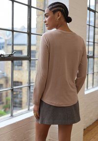 Long-sleeve, light beige top with a rounded neckline paired with a gray textured skirt featuring a subtle houndstooth pattern.