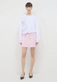 Top bianco a maniche lunghe con rose in tessuto texturizzato sulla sinistra; abbinato a una minigonna rosa chiaro con vita regolabile e fessure laterali.