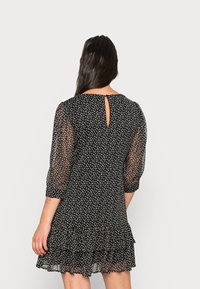 Schwarzes Kleid mit weißen Polka-Dots, durchsichtigen Puffärmeln, einem Rückenausschnitt mit Schlitzverschluss und einem Rüschensaum. Leichter Stoff.