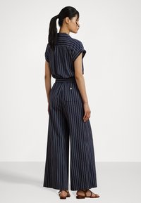 Marine gestreepte jumpsuit met korte mouwen, wijde pijpen en een opgerekte taille. Heeft een kraag aan de achterkant en een subtiele merkteken detail bij de taille.