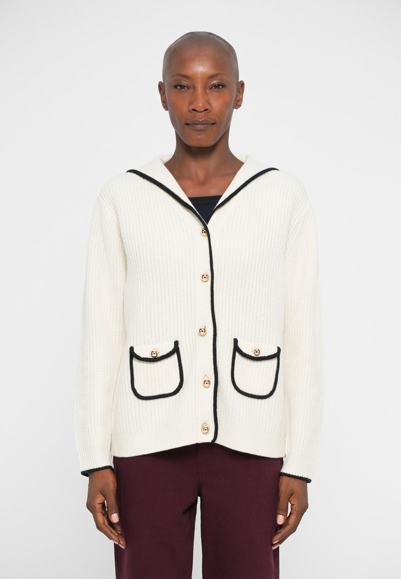 Cardigan din material tricotat cu model de waffle, de culoare crem cu detalii negre, având glugă, nasturi aurii și două buzunare frontale cu margini curbe.