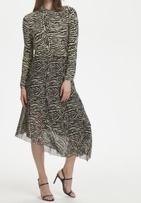 Langärmliges Kleid mit Zebramuster, das einen enganliegenden Oberteil und einen fließenden, durchsichtigen Rock hat; die Farben sind Beige und Schwarz.
