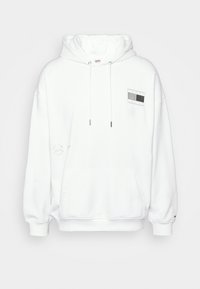 Felpa bianca con tasca frontale, cappuccio regolabile con lacci, e un logo rettangolare grigio e nero sul petto. Materiale in cotone con una consistenza morbida.